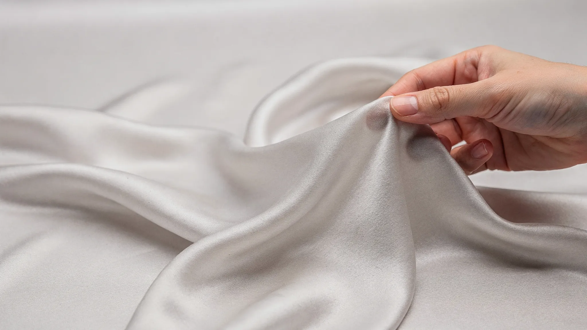 Close-up of viscose rayon fabric draped in soft folds, showing a smooth surface and fluid drape, with a hand gently pinching the fabric to demonstrate softness.